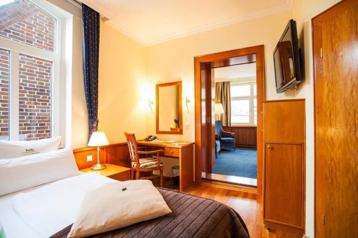 A hotel room with a bed, desk, chair, and a television on the wall.