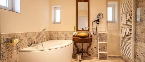 A bathroom with a large bathtub, a sink with a mirror, a towel rack, and a shower area.