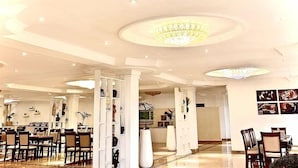 A spacious hotel lobby with high ceilings, chandeliers, and a seating area with tables and chairs. - Hotel De Leopol International (Addis Ababa)