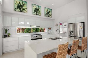 A modern kitchen with white cabinetry, a central island, and a stainless steel refrigerator. - Palm Haven Coolum Beach (Sunshine Coast)
