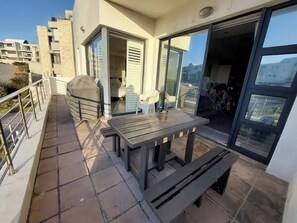 Een balkon met een tafel, stoelen, een barbecue en een schuifpui naar een binnenruimte.