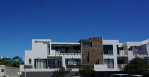 Een modern meerlaags gebouw met balkons, grote ramen en een bord waarop 'Sunset Bay' staat.