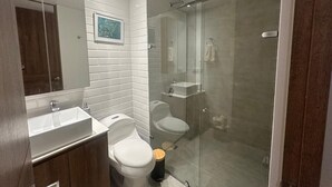 Et moderne badeværelse med en glasafskærmet brusekabine, en hvid vask og et toilet.