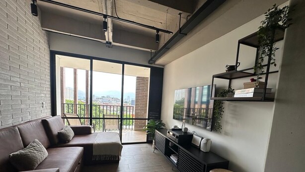 En moderne stue med sofa, lænestol, fjernsyn og en balkon med udsigt over byen.