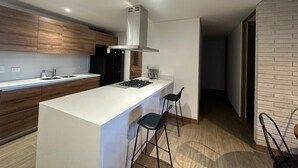 Et moderne køkken med en central ø, barstole og et rustfrit stål emfang.