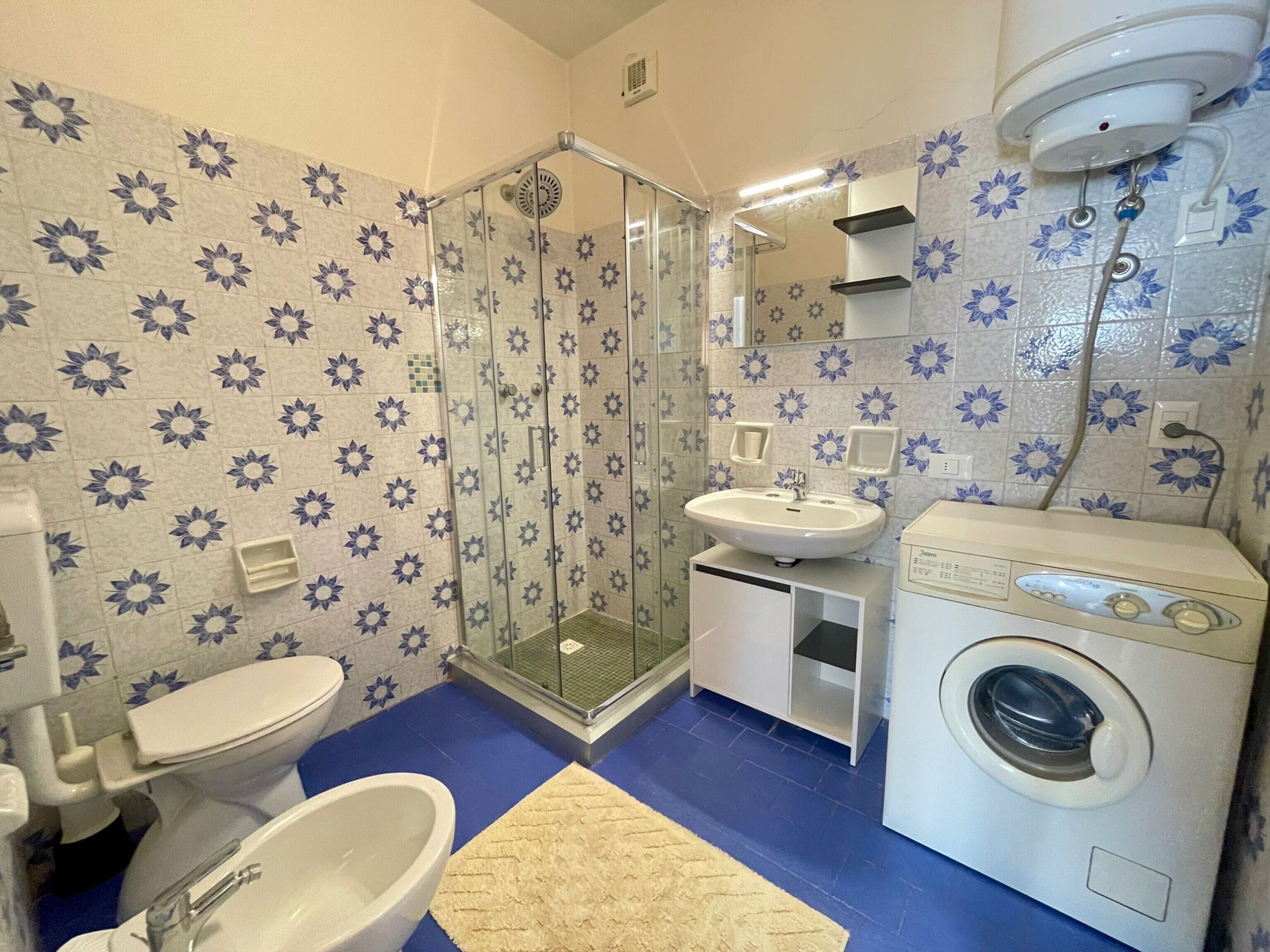 A bathroom with a shower, toilet, sink, and washing machine.