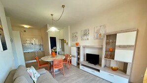 A modern living room with a sofa, dining table, chairs, a TV, and a fireplace. - Cozy Flat 370m From the Beach (Caorle)