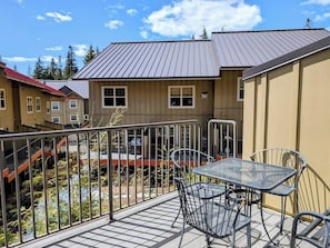 A balcony with a metal table and chairs, a view of a building with a red roof, and a metal railing. - Chalet 41 at The Official Collins Lake Resort (Government Camp)