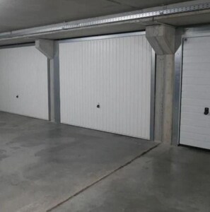 Eine Parkgarage mit drei weißen Garagentoren, Betonpfeilern und einem ebenen Betonboden.
