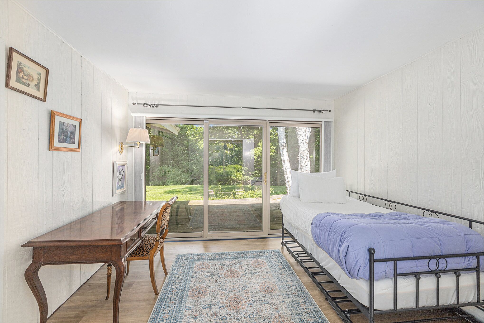 A bedroom with a bed, a desk, a chair, a window, and a view of the outdoors.