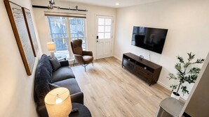 A modern living room with a sofa, armchair, TV, and a small table with a lamp. - The Accessible Atom | Historic Main (Saint Charles)