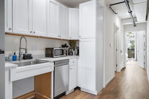 A modern kitchen with white cabinetry, stainless steel appliances, and a wooden floor. - The Accessible Atom | Historic Main (Saint Charles)