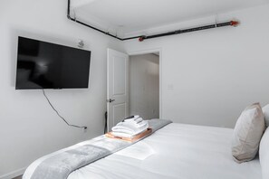 A bedroom with a bed, a flat-screen TV mounted on the wall, and a door leading to another room. - The Accessible Atom on Historic Main (Saint Charles)