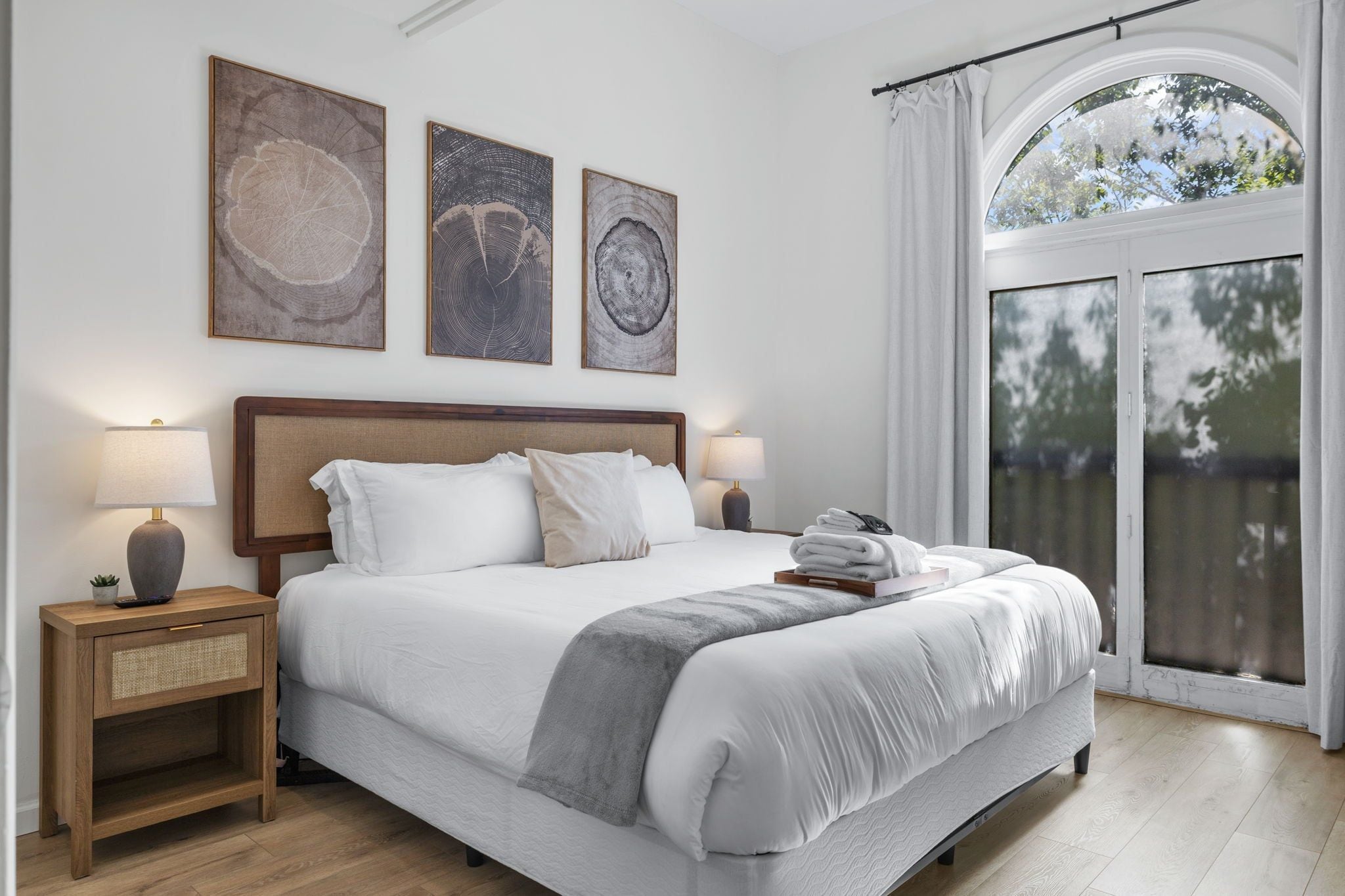 Une chambre d’hôtel avec un grand lit, deux tables de chevet avec des lampes et trois œuvres d’art encadrées accrochées au mur.