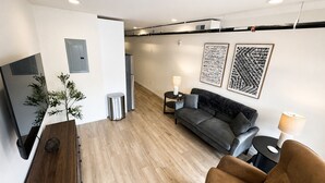 A modern living room with a sofa, a brown armchair, a small side table, a plant, and artwork on the wall. - The Accessible Atom | Historic Main (Saint Charles)