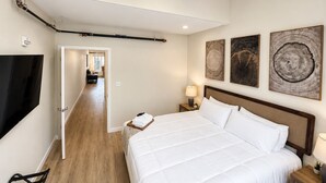 A hotel room with a large bed, a TV, a wooden floor, and artwork on the wall. - The Accessible Atom | Historic Main (Saint Charles)