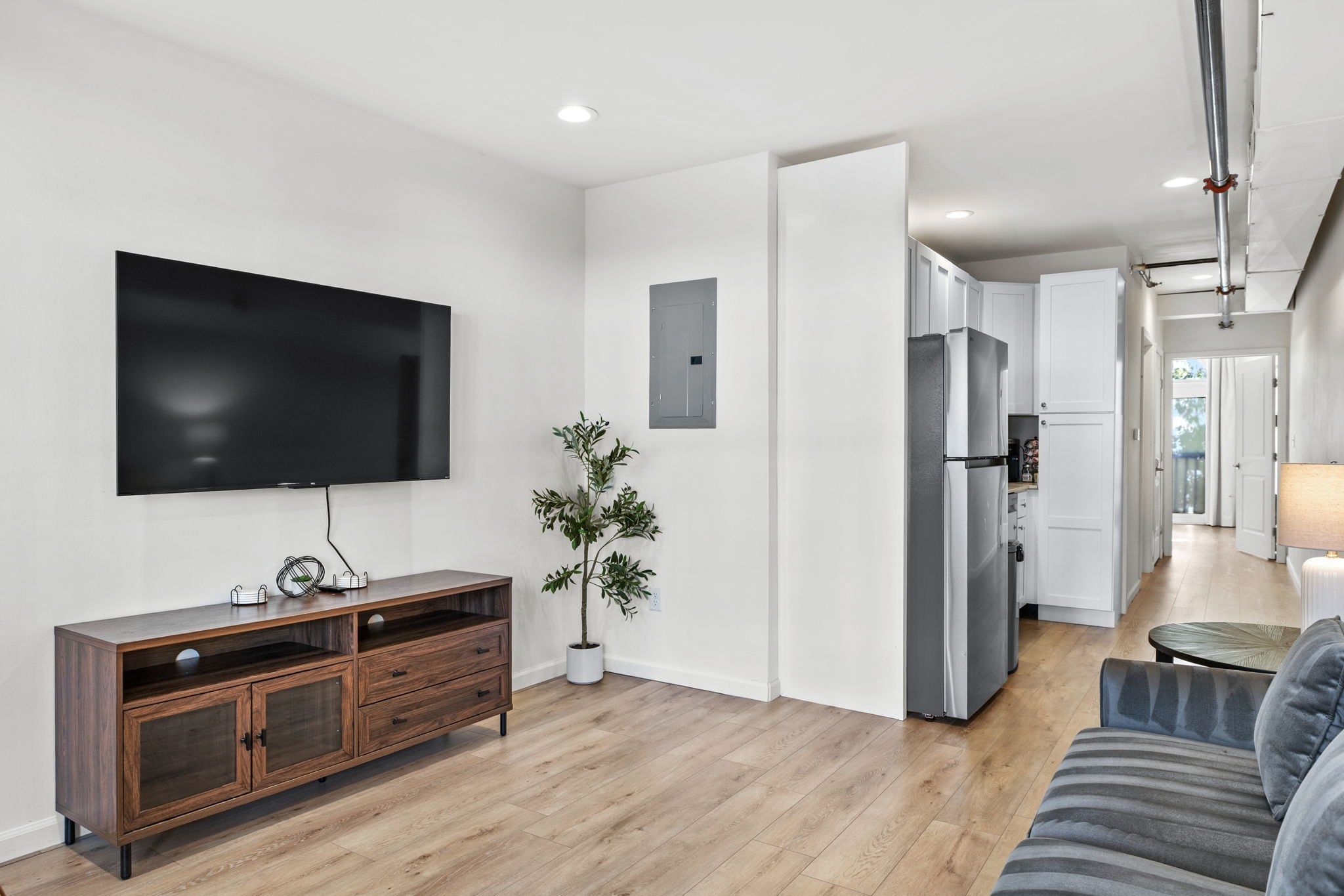 Un salon moderne avec un téléviseur à écran plat, un meuble en bois, une plante en pot et un canapé gris.