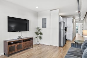 A modern living room with a flat-screen TV, a wooden cabinet, a potted plant, and a grey sofa. - The Accessible Atom | Historic Main (Saint Charles)