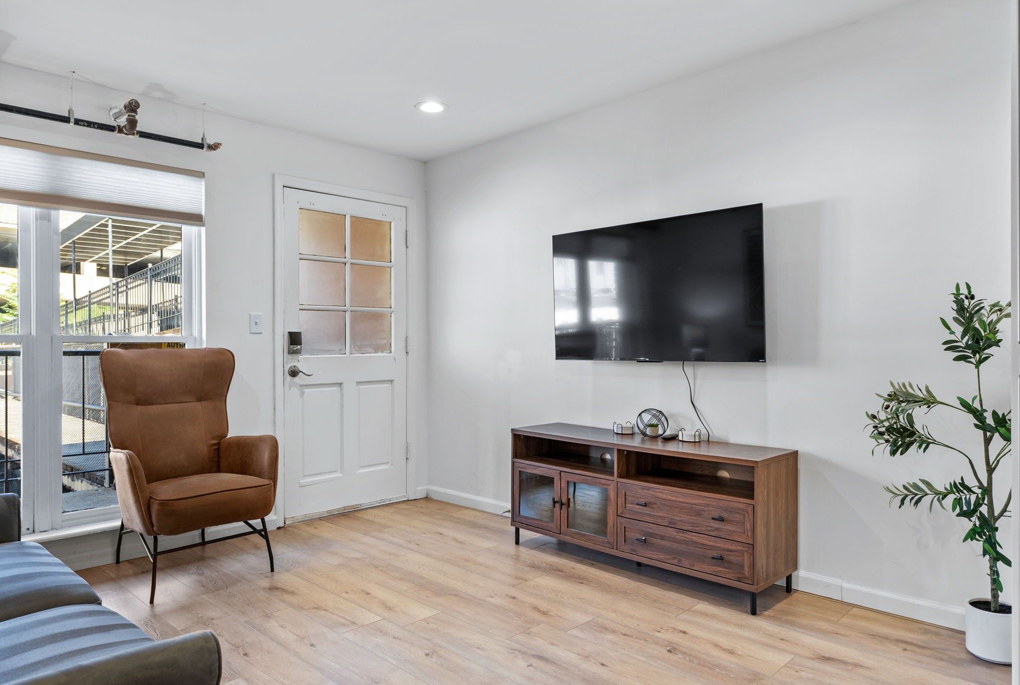 Bright living room with a wall-mounted TV, media console, armchair, and exterior door.