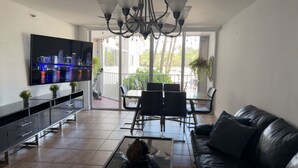 Ein modernes Wohnzimmer mit einem Flachbildfernseher, einem Ledersofa, einem Esstisch mit Stühlen und einer Kristallleuchtre.