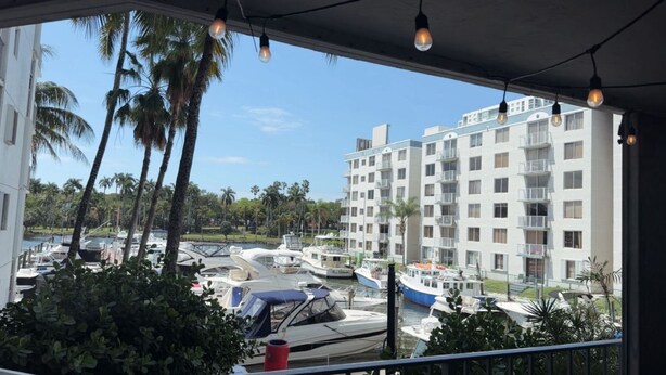 Blick auf eine Marina mit vertäuten Booten, ein mehrstöckiges Gebäude mit Balkonen und Palmen im Hintergrund.