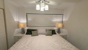 Ein Schlafzimmer mit einem Bett, zwei Nachttischen mit Lampen, einem großen Spiegel und einem Deckenventilator.