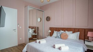Une chambre à coucher avec un lit, des tables de chevet, un miroir, une porte et une horloge murale.