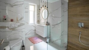 Une salle de bain avec un mur en marbre, une cabine de douche en verre, des toilettes et un lavabo.
