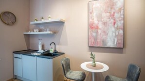 A modern kitchen with a built-in stove, a sink, and a small island. There are two chairs and a table with a vase of flowers. A large abstract painting is on the wall. - Prime City Center Studio in Split - Walk to Diocletian's Palace (Split)
