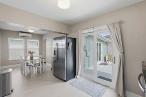Una cocina moderna con refrigerador, mesa de comedor, sillas y una puerta corrediza de vidrio que da a un balcón.