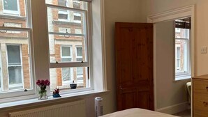 Ein Schlafzimmer mit Bett, Heizkörper, einem Vorhangfenster, einer Holztür und einem Schminktisch.