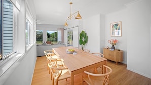 A dining area with a wooden table, chairs, pendant lighting, a plant, and a cabinet. - The Lookout – Resort Living with Panoramic Views Over Diamond Beach (Diamond Beach)