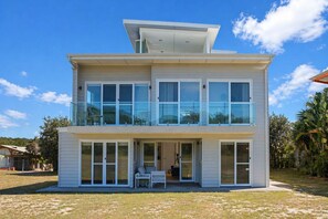 A modern two-story house with large windows, a balcony, and a covered patio area.