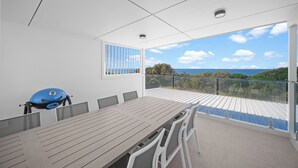 A modern outdoor dining area with a large table and chairs, a grill, and a view of the ocean. - The Lookout – Resort Living with Panoramic Views Over Diamond Beach (Diamond Beach)