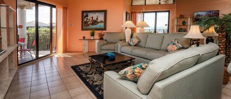 A living room with a sofa, coffee table, and lamps. There is a balcony with a view outside.