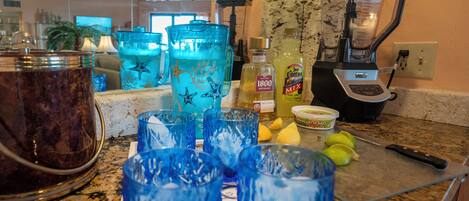 Una encimera de cocina con una licuadora, vasos y una tabla de cortar con limones.