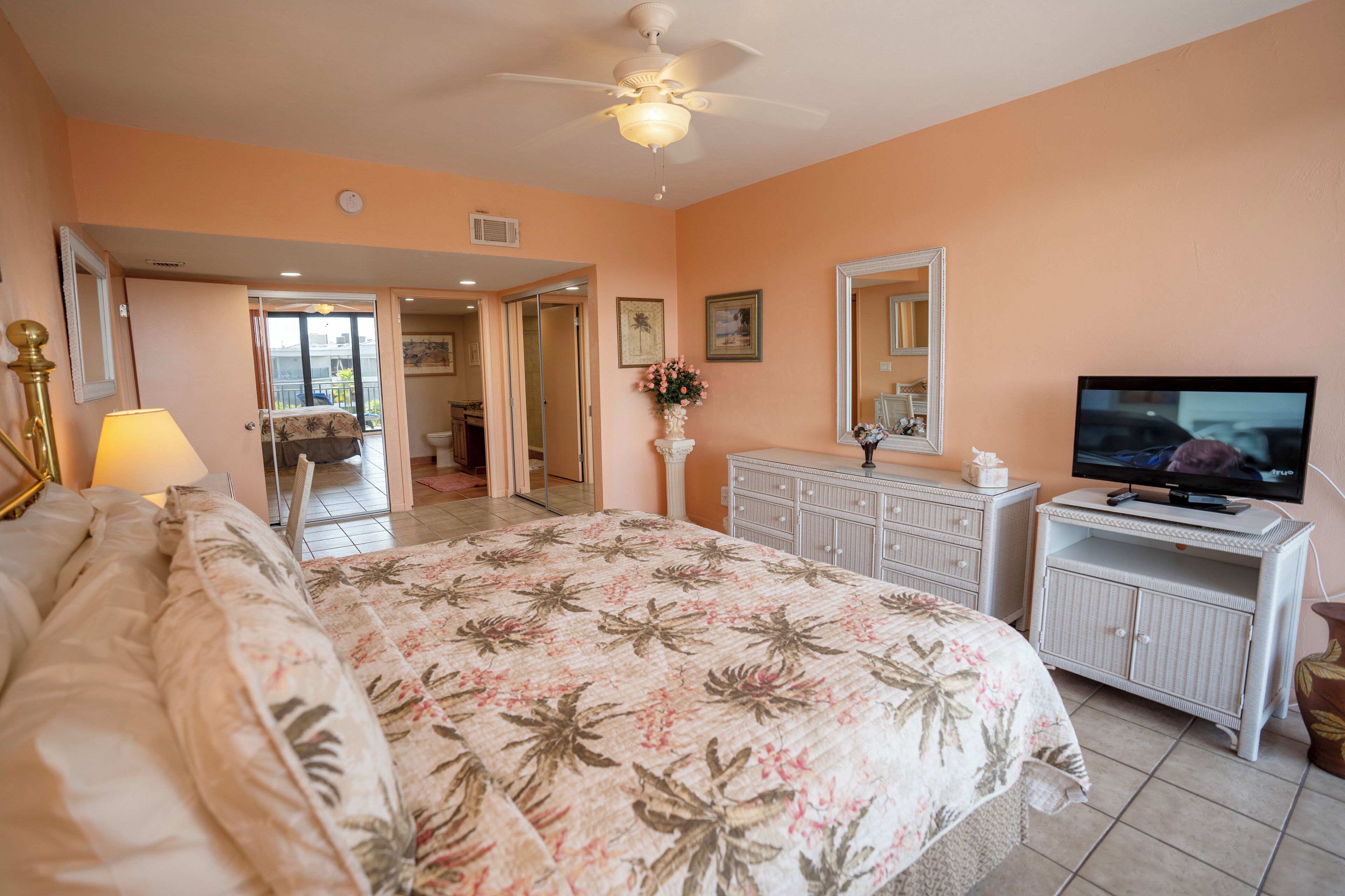 A bedroom with a bed, a television, a dresser, and a ceiling fan.