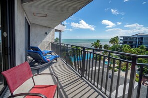 A balcony with a red chair and blue lounge chairs, overlooking a pool and ocean. - Key West Paradise Found - Experience the Best Views at 1800 Atlantic (Key West)