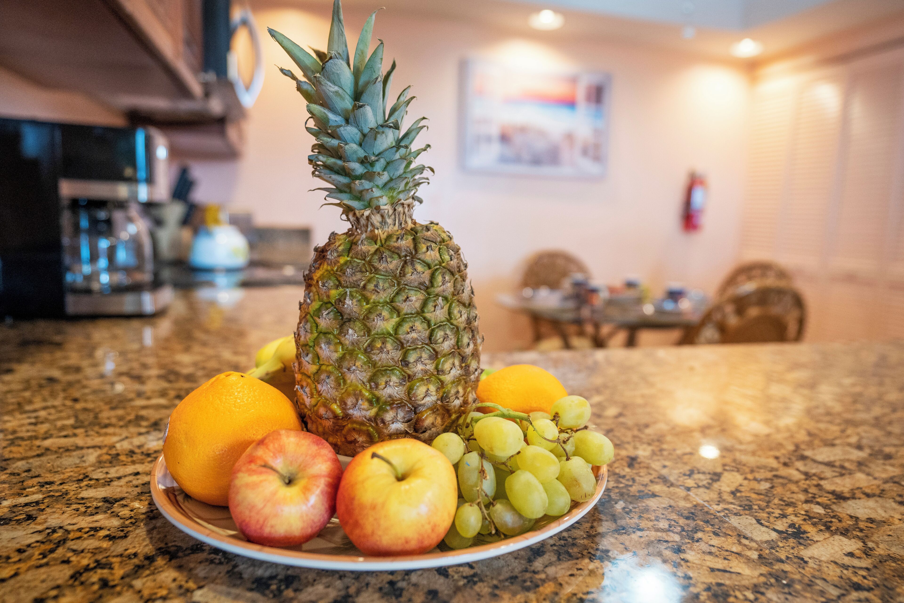 Une assiette de fruits est posée sur un comptoir de cuisine, avec un four à micro-ondes, une cuisinière et un coin repas en arrière-plan.