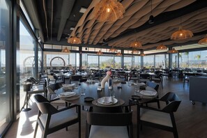 A modern restaurant with large windows, round tables, and hanging wicker light fixtures. - Designer Villa with Heated Pool on Santa Rosalia Lake Resort (Torre-Pacheco)