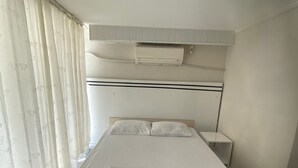 Ein Einzelbett mit Kopfteil, ein Nachttisch und ein Fenster mit Vorhängen.