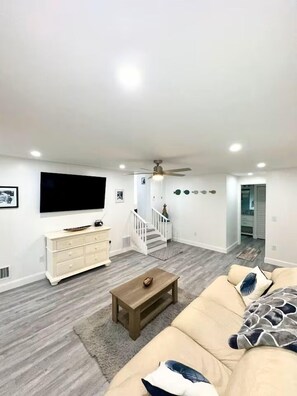 A modern living room with a flat-screen TV, a beige sofa, a wooden coffee table, and a staircase leading to another level.