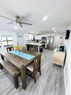 A modern kitchen with a dining area, a ceiling fan, and a view of the outdoors.