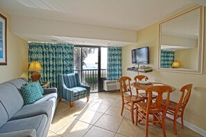 Ein Zimmer mit einer Couch, Sesseln, einem Esstisch, einem Fernseher und einem großen Spiegel.