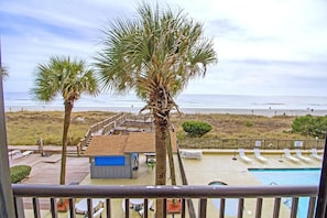 Blick vom Balkon auf einen Strand, einen Pool, Palmen und einen Strand im Hintergrund.