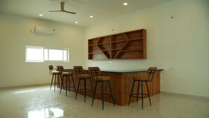 A bar area with a wooden counter and bar stools, a ceiling fan, and a window.