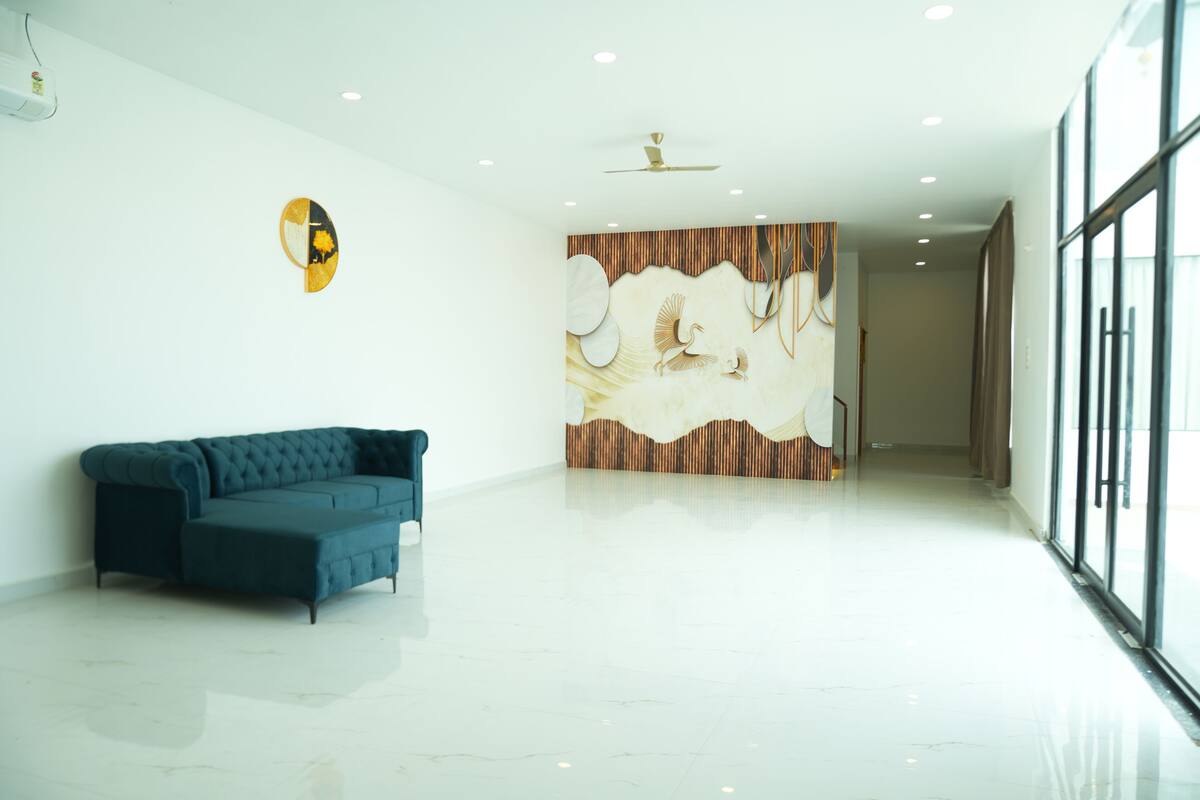 A spacious room with a modern design, featuring a blue sofa, a wall mural, and a ceiling fan.