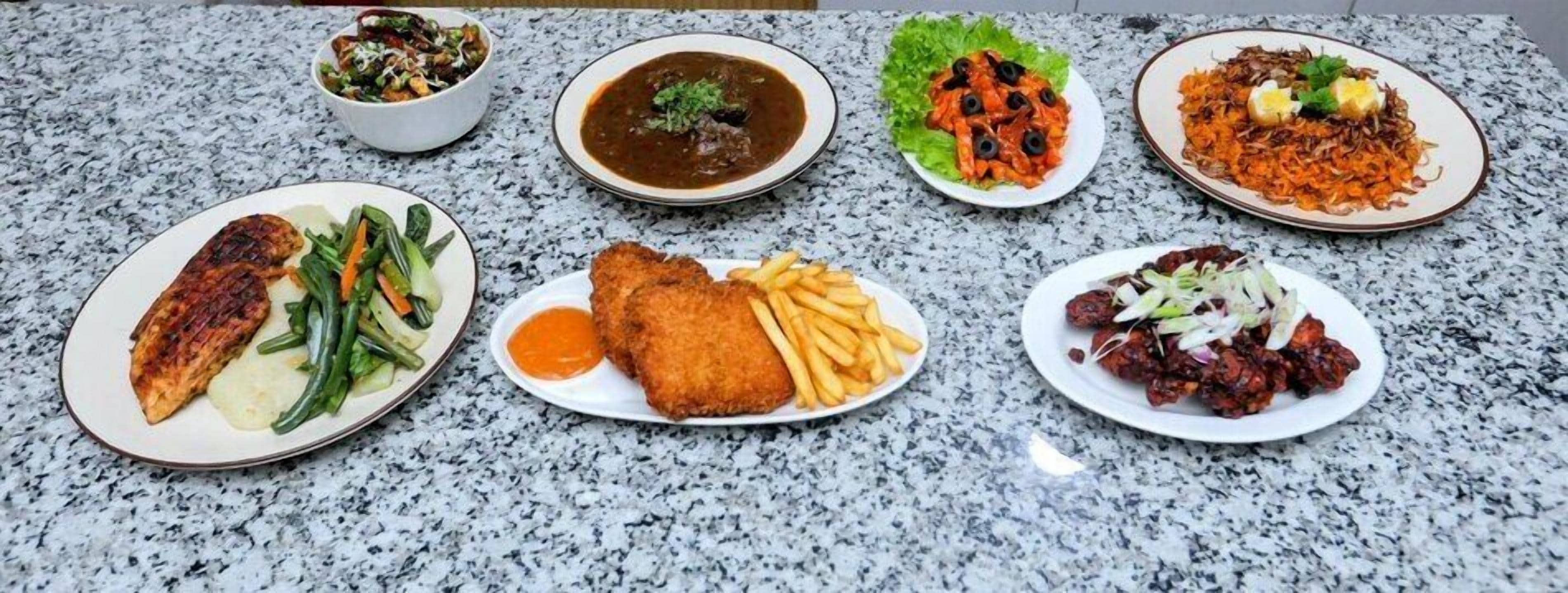 Una encimera de granito con varios platos, incluyendo pescado a la parrilla, papas fritas y verduras mixtas.