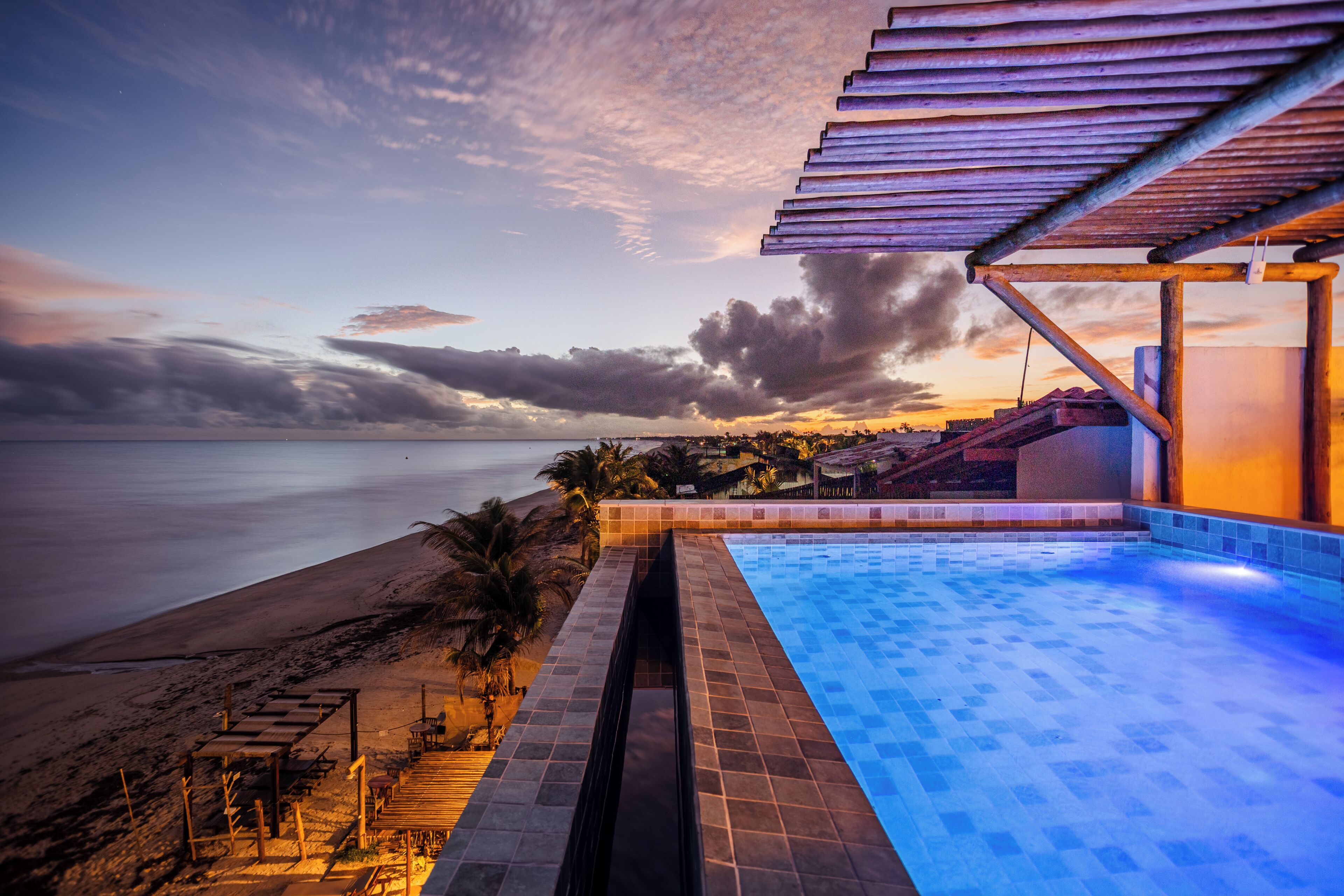 A poolside view with a beach and sunset.