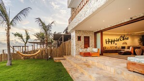 A two-story building with a stone facade, a hammock in the yard, and a sign reading 'Hippie Chic' in the entrance. - Beachfront retreat in Preá, with pool, rooftop, massage room and gym. (Caiçara)